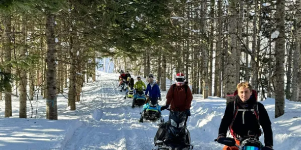 Group of snowmobile riders paused in a snowy forest clearing